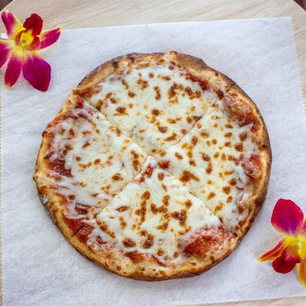 A small, round cheese pizza, sliced into four pieces, on parchment paper with two orchids.