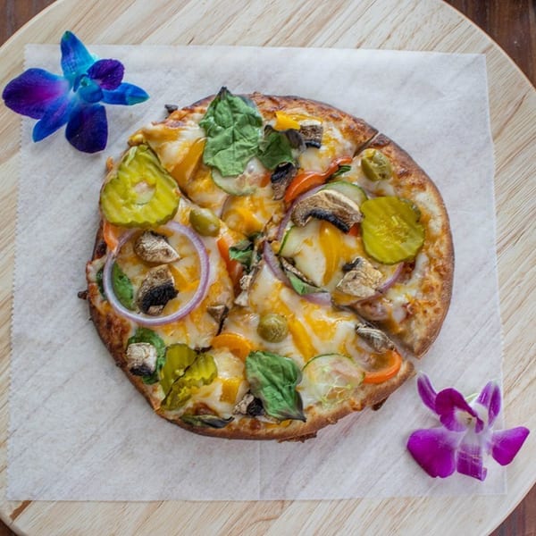 A small, round pizza with various toppings and two purple orchids on a wooden board.