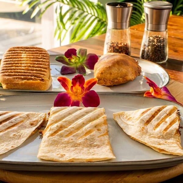 Grilled sandwiches, pastries, and quesadillas on plates with orchids, salt, and pepper shakers.